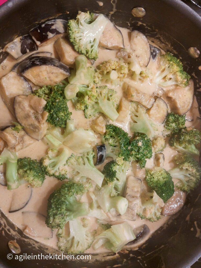 In a pot, layering a vegetable curry, quartered aubergine and broccoli florets in a curry sauce