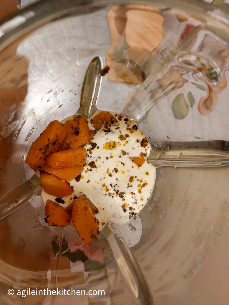 Looking from above into a standing mixer, roasted butternut squash, chili flakes and cream, ready to be mixed.