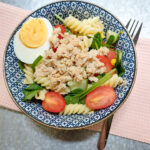 A blue patterned bowl with lemon salmon pasta salad, underneath the bowl a pink, textured cloth and a fork