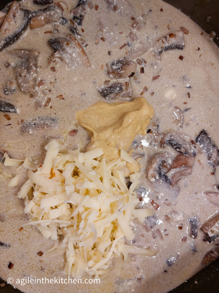 A close up of mushroom sauce where mustard and shredded cheese have just been added