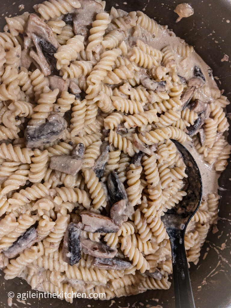 In a pot, mushroom sauce mixed with cooked fusilli pasta.