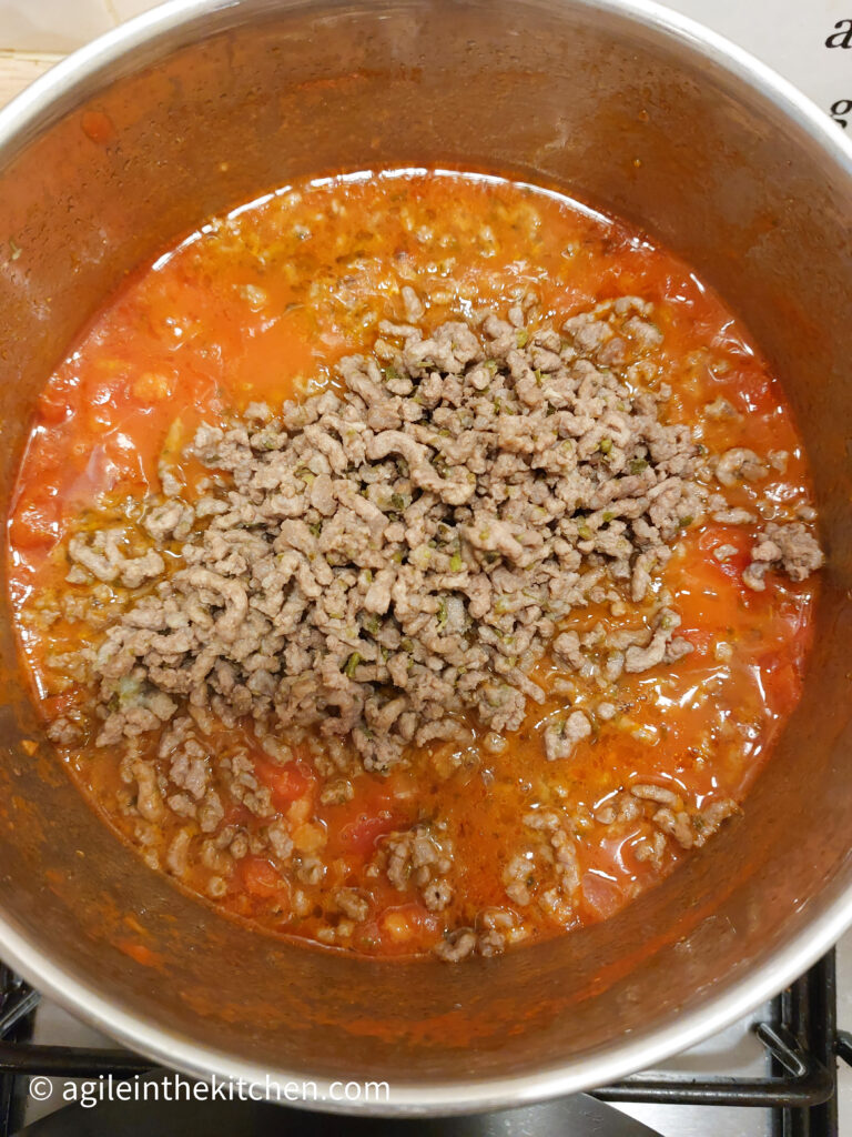 In a pot, tomato sauce at the bottom and cooked mince meat on the top