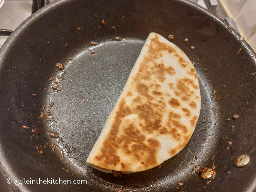 In a frying pan, a folded quesadilla, with a baked top