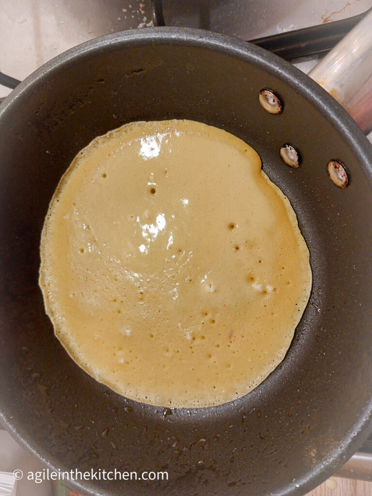 In a frying pan, a pancake is being cooked, with the top almost done and ready to turn