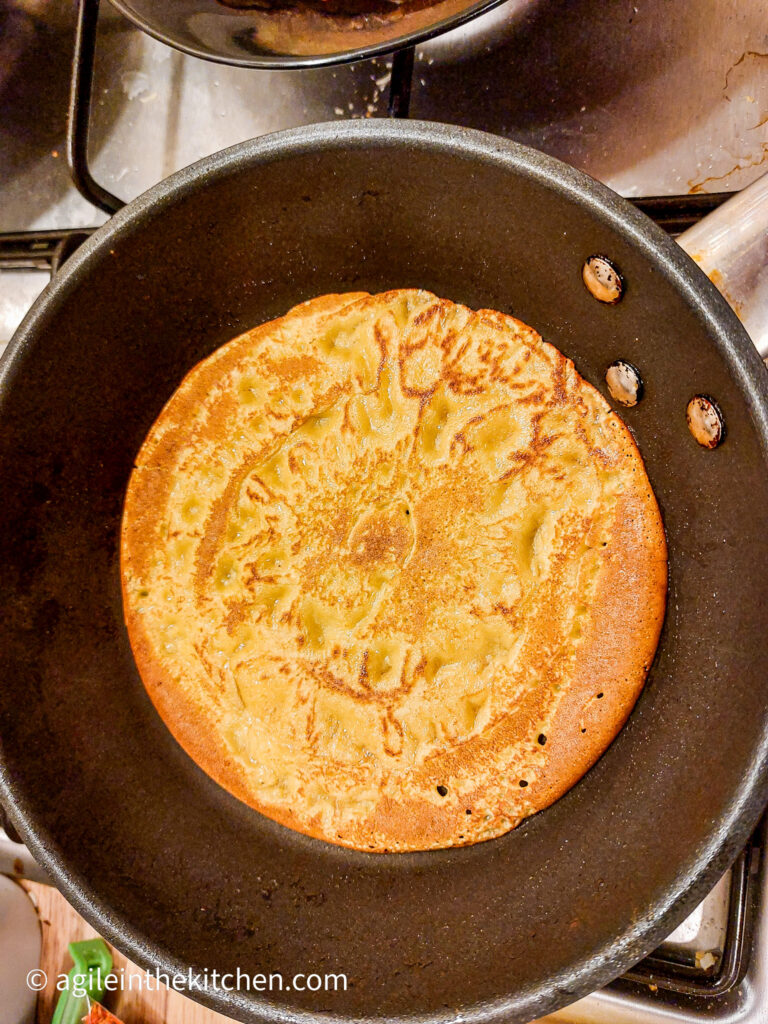 In a frying pan, a pancake is being cooked, with the top almost done