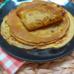 In wicker basket, a black plate with saffron pancakes piled up with the top one folded in fours.