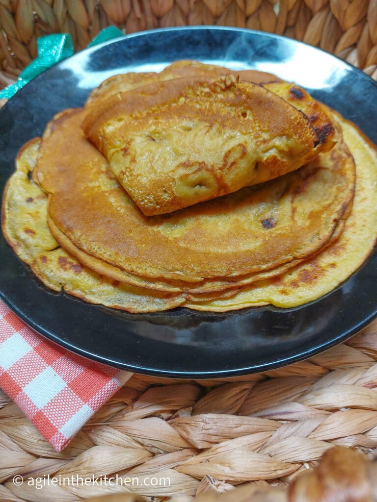 In wicker basket, a black plate with saffron pancakes piled up with the top one folded in fours.