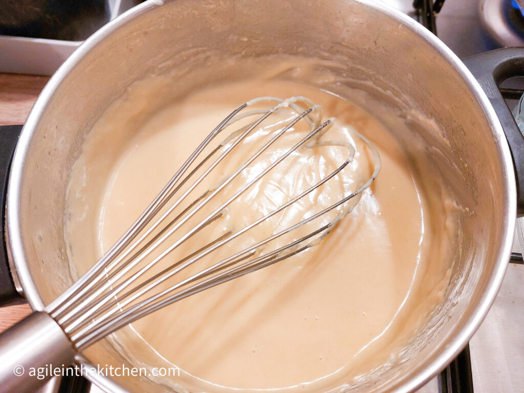 A pot with cheese sauce for mac n cheese and a steel whisk