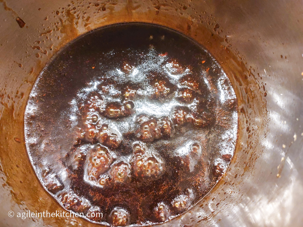 A pot filled with Teriyaki sauce that is cooking, forming bubbles on the surface.