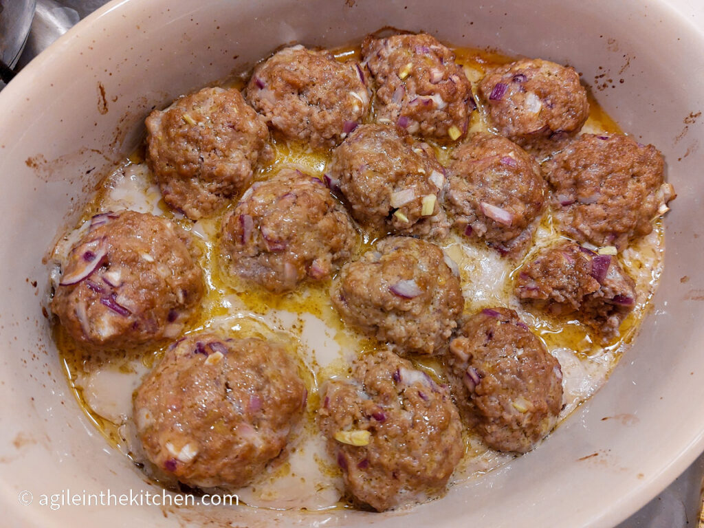 In an oven dish with a white interior, fifteen barbecue meatballs are cooked.