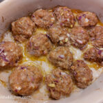 In an oven dish with a white interior, fifteen barbecue meatballs are cooked.