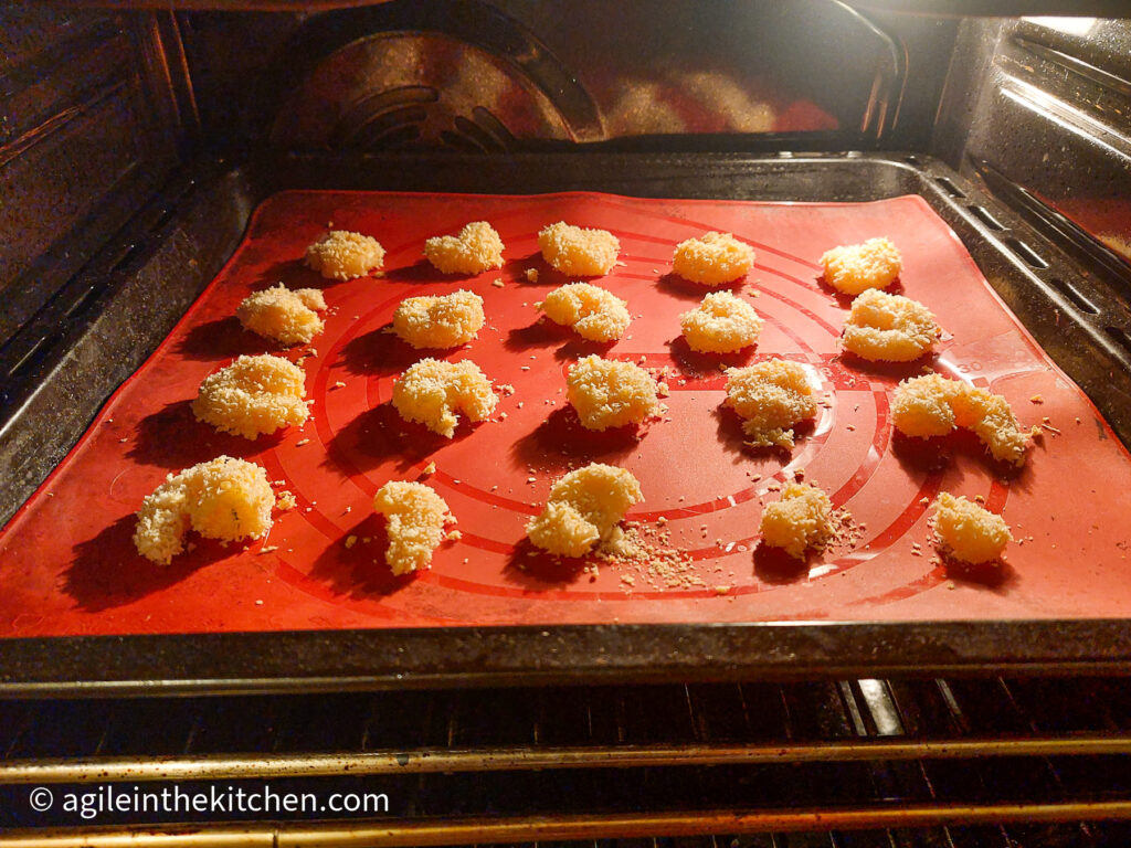 A photography taken from the oven. On a red silicone cookie sheet, there four rows with five columns of crispy prawns ready to be cooked.
