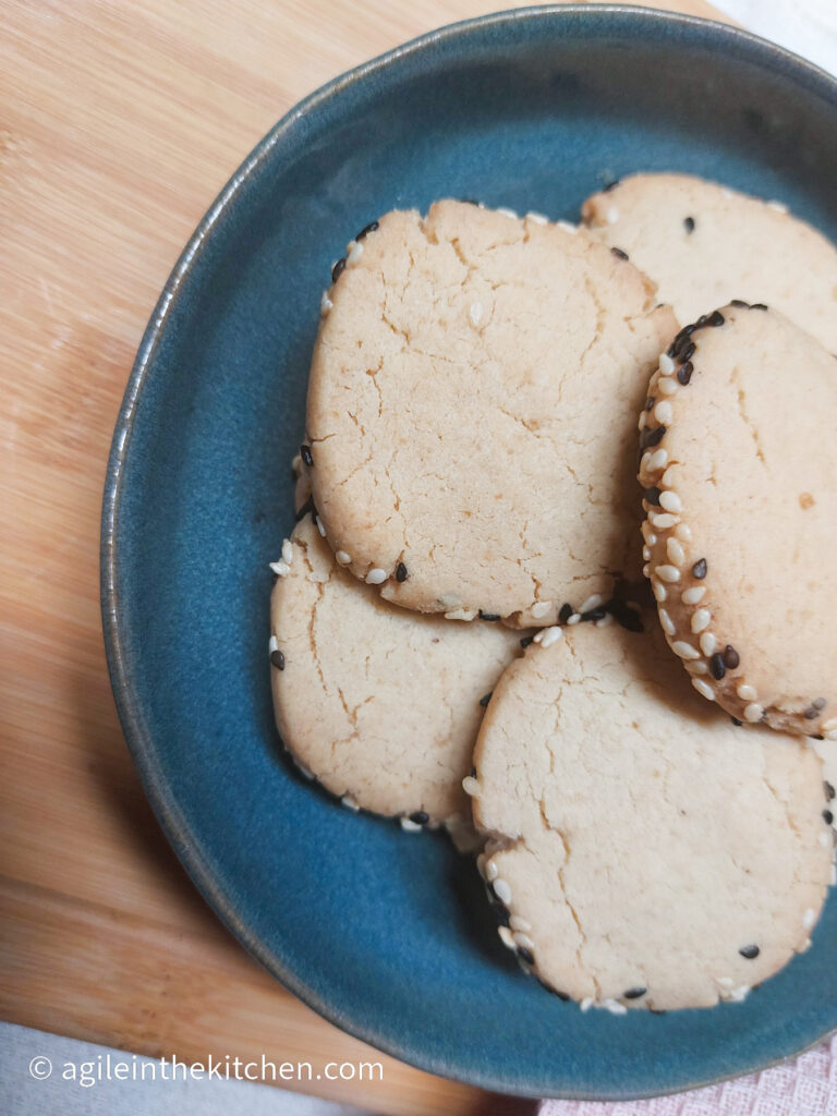 On a wooden background, a blue plate with tahini cookies piled up.