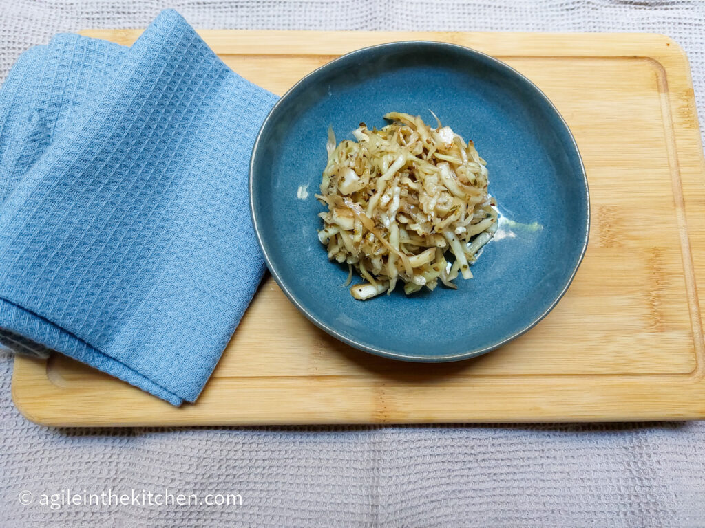 On a wooden cutting board, a blue, textured folded cloth napkin, a blue small plate with a pile of cabbage salad
