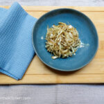 On a wooden cutting board, a blue, textured folded cloth napkin, a blue small plate with a pile of cabbage salad