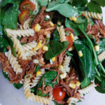 In a bowl, pulled pork pasta salad with pasta, canned corn, half cut tomatoes, spinach leaves and pulled pork