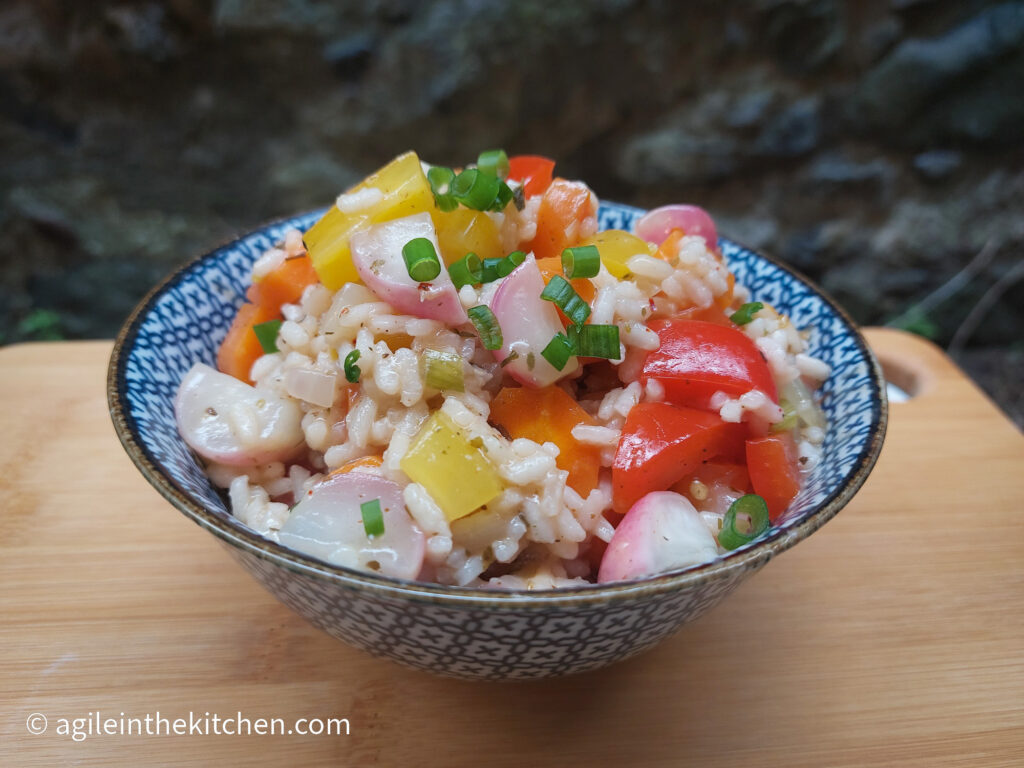 On a wooden cutting board, a blue patterned bowl with rainbow risotto salad