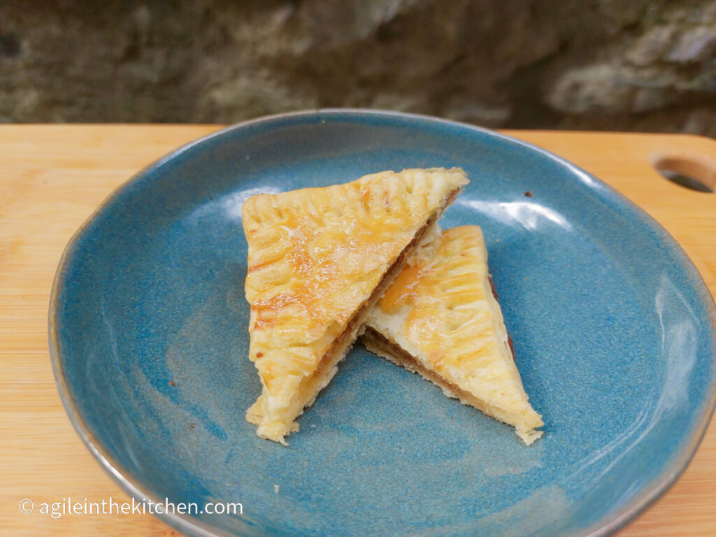 On a wooden cutting board, a blue plate with a cinnamon rectangle cut in two triangles one half on top of the other.