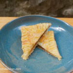 On a wooden cutting board, a blue plate with a cinnamon rectangle cut in two triangles one half on top of the other.