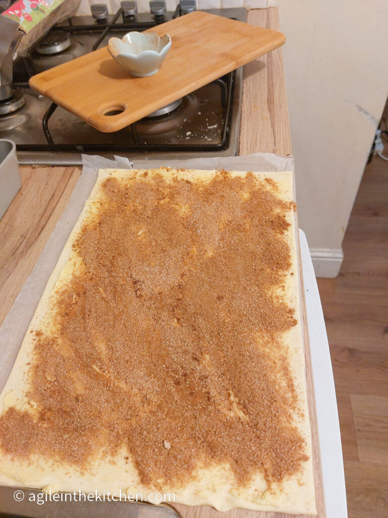 A photo taken from slightly above with a sheet of rolled out puff pastry covered in butter and cinnamon mix.