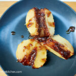 On a wooden cutting board a black matte plate with a fragrant baked apple cut in three pieces.