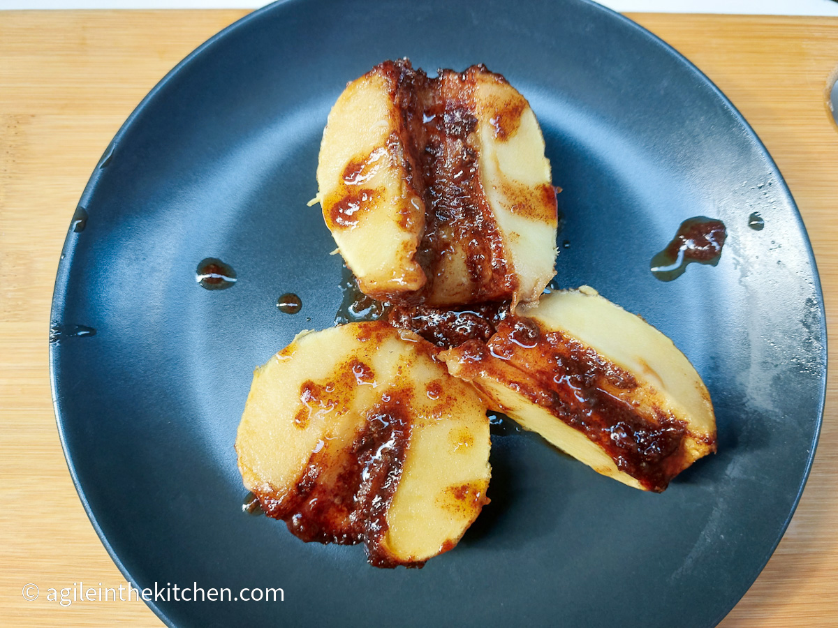 On a wooden cutting board a black matte plate with a fragrant baked apple cut in three pieces.