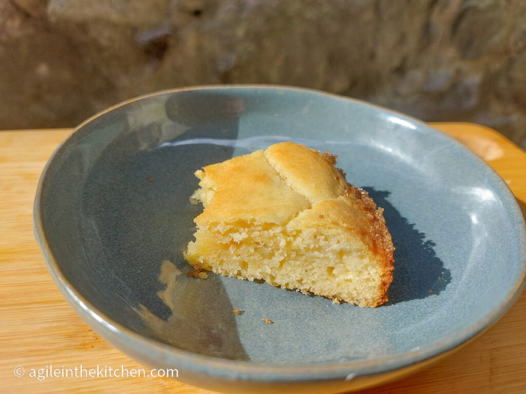 On a wooden cutting board, a blue plate with a half eaten slice of white chocolate cake.
