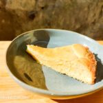 On a wooden cutting board, a blue plate with a slice of white chocolate cake.