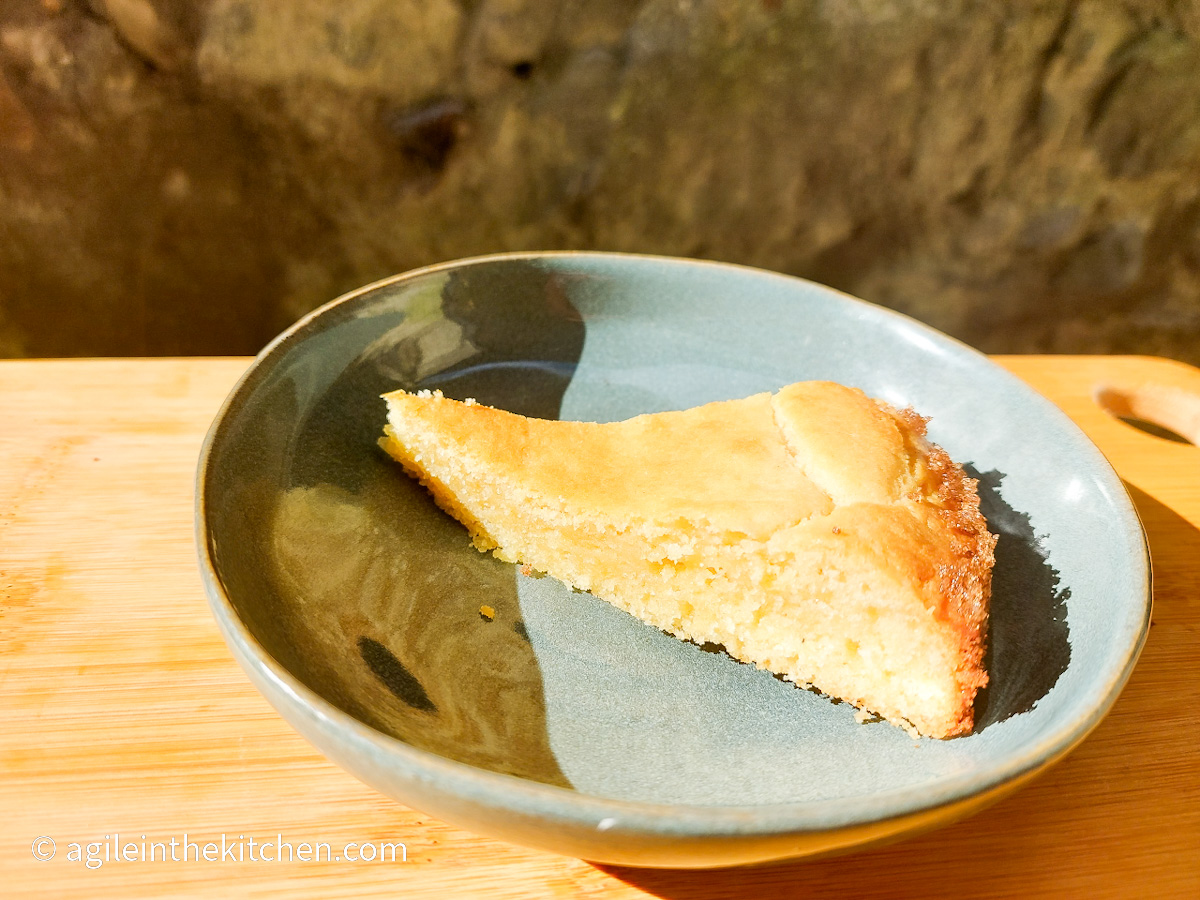 On a wooden cutting board, a blue plate with a slice of white chocolate cake.