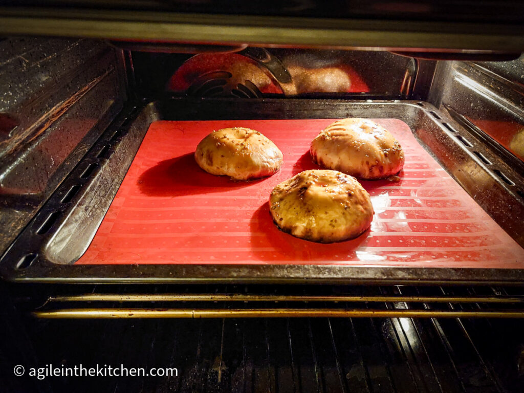 A photo taken in to an oven, a cookie sheet with a red silicon sheet, three mushrooms caps facing down.