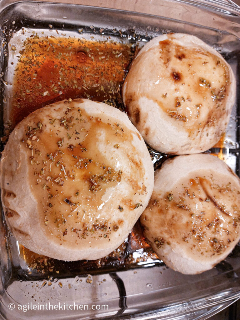 A shallow glass bowl with three mushrooms caps resting in a marinade.
