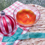 A glass bowl with saffron syrup next to a red striped bauble, underneath is a red gingham cloth in a shallow basket