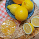 A photo taken from above of a blue patterned bowl with lemons, a sliced lemon on the side and a bowl of honey, all in a shallow basket with a red gungham cloth at the bottom.