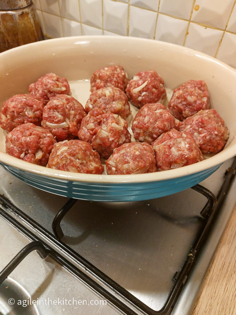 In a blue oven proof dish, raw Asian meatballs ready to be baked in the oven