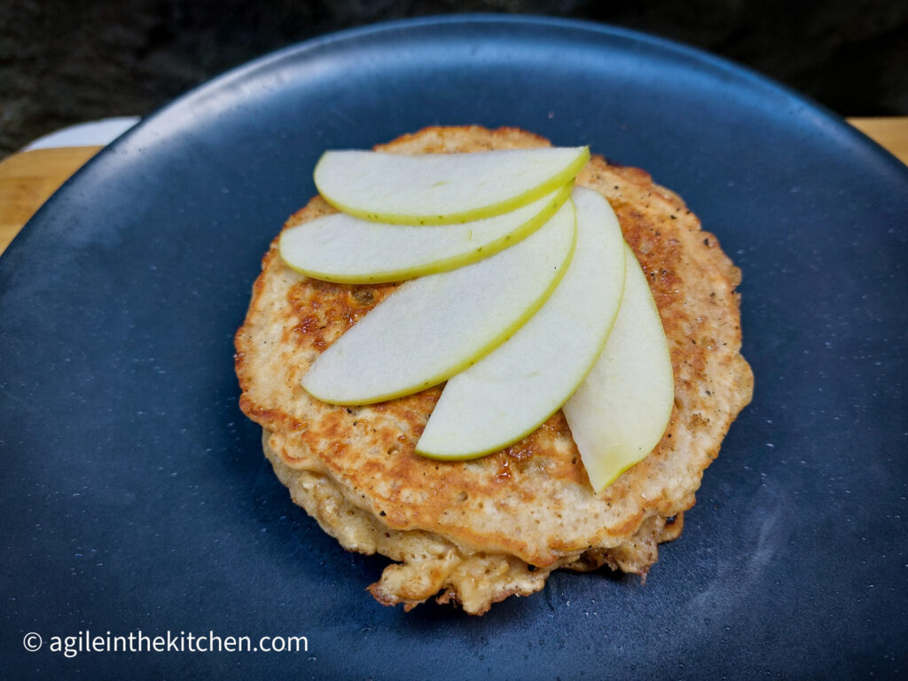 On a blue matte plate, a oat and brown sugar pancake with five thinly sliced of apples on top