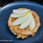 On a blue matte plate, a oat and brown sugar pancake with five thinly sliced of apples on top