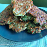 On a blue textured placemat, a black matte plate, piled high with broccoli pancakes